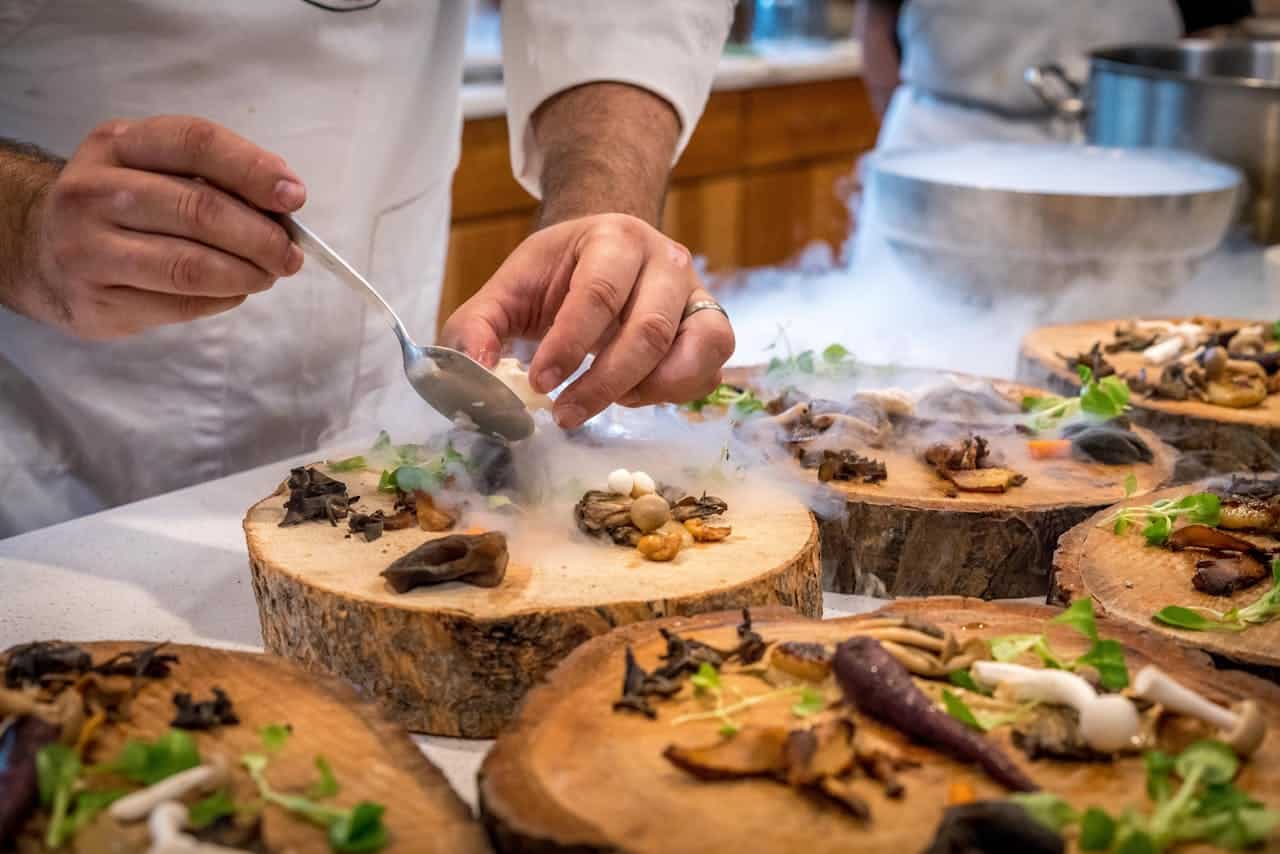 services-02 A chef artfully plating a gourmet dish with mushrooms and greens on wood slices.